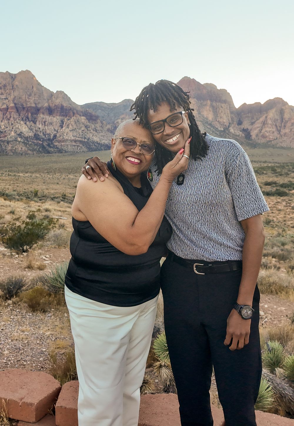 Two women smiling and embracing at Red Rock Canyon Nevada with scenic desert mountains in the background.