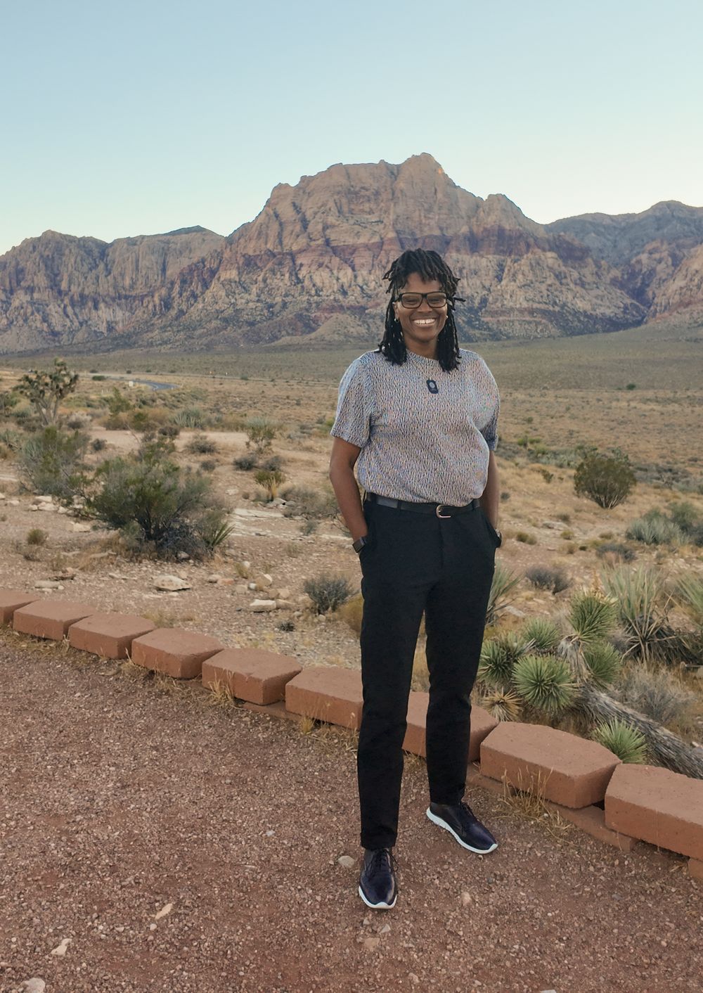Woman smiling at Red Rock Canyon desert landscape with red sandstone mountains in Nevada.