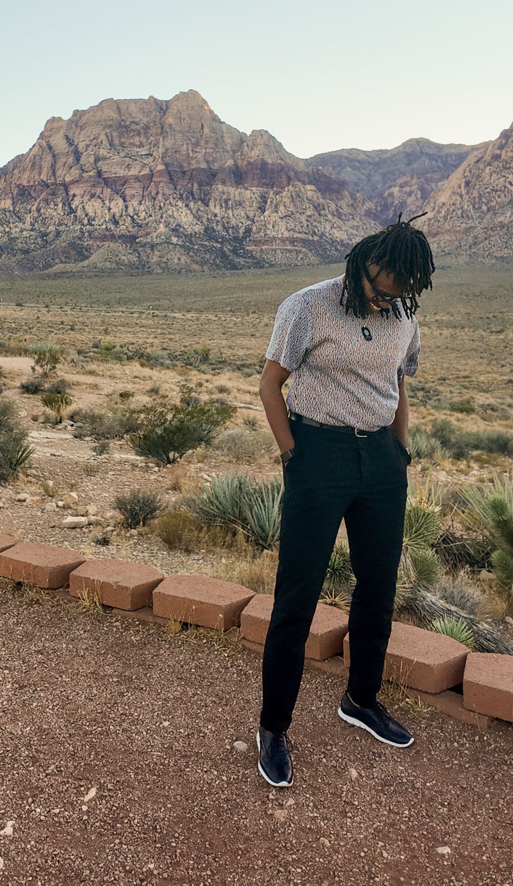 Young man with dreadlocks standing at Red Rock Canyon with dramatic rocky mountains behind him.