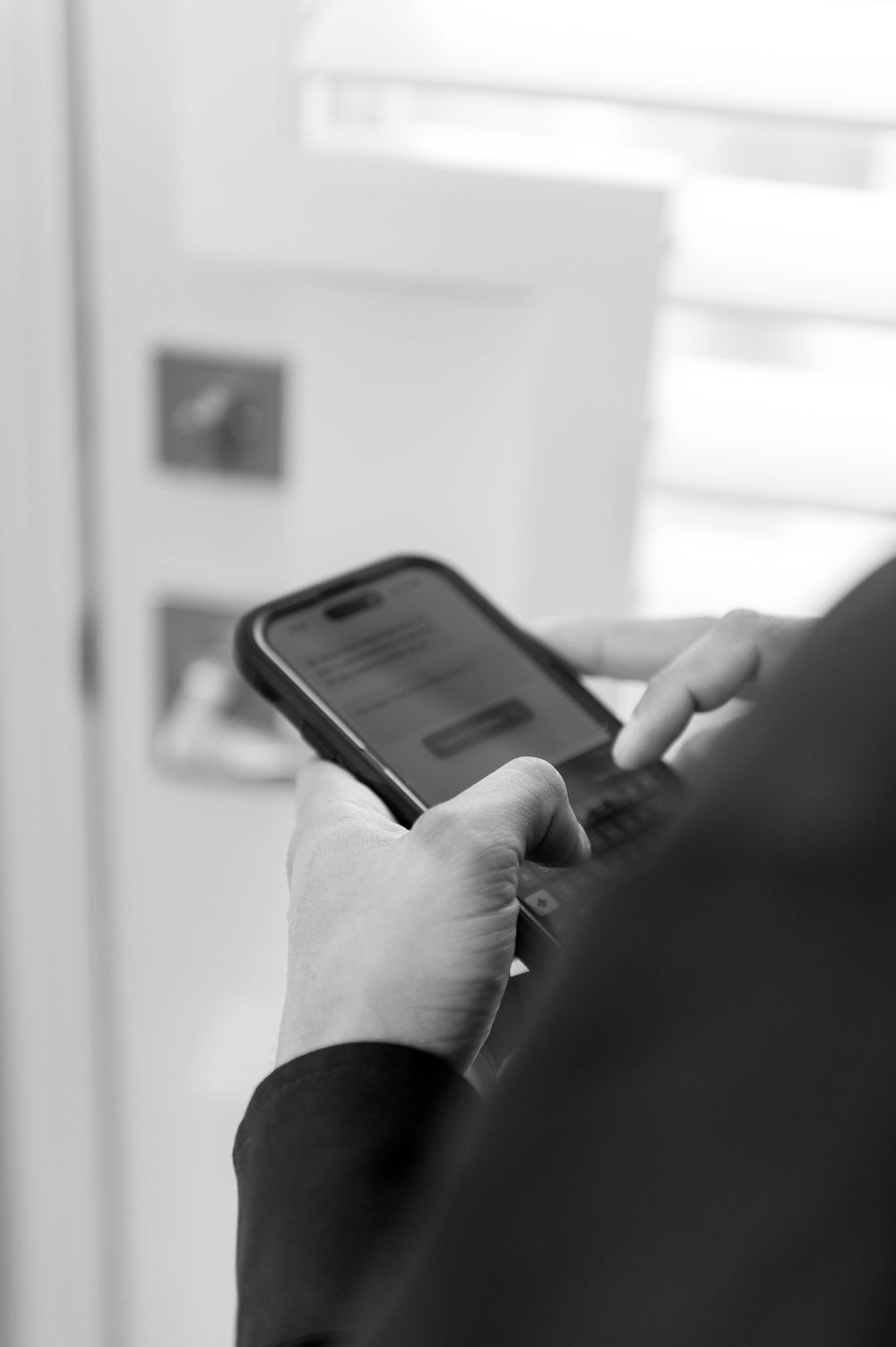 Close-up black and white photo of hands holding a smartphone with a dark case.