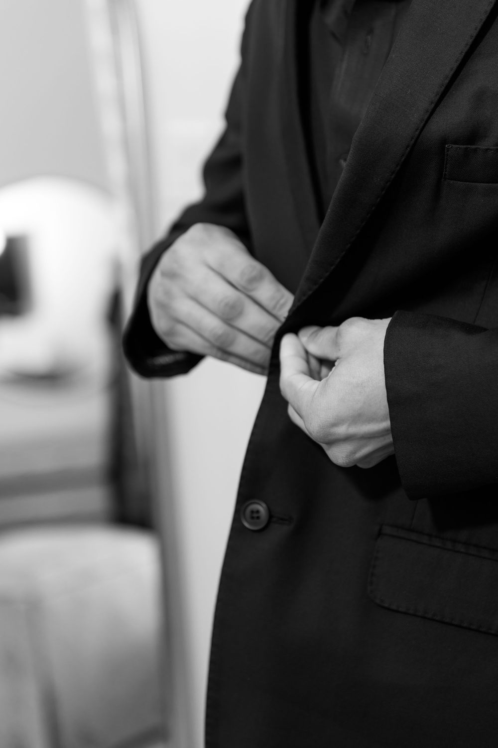 Close-up of groom buttoning black suit jacket during wedding day preparations.