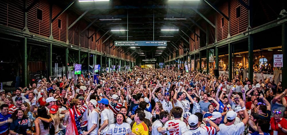 Large crowd of USA fans celebrating at an indoor sports viewing event.