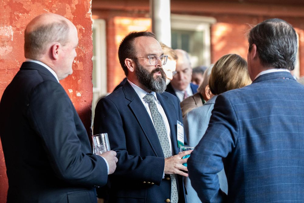 Three professionals in suits networking at a formal business event, engaged in conversation outdoors.