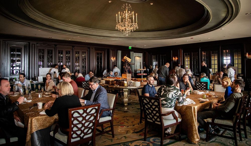 Elegant restaurant dining room with chandelier, dark wood paneling, and guests seated at tables with gold tablecloths.
