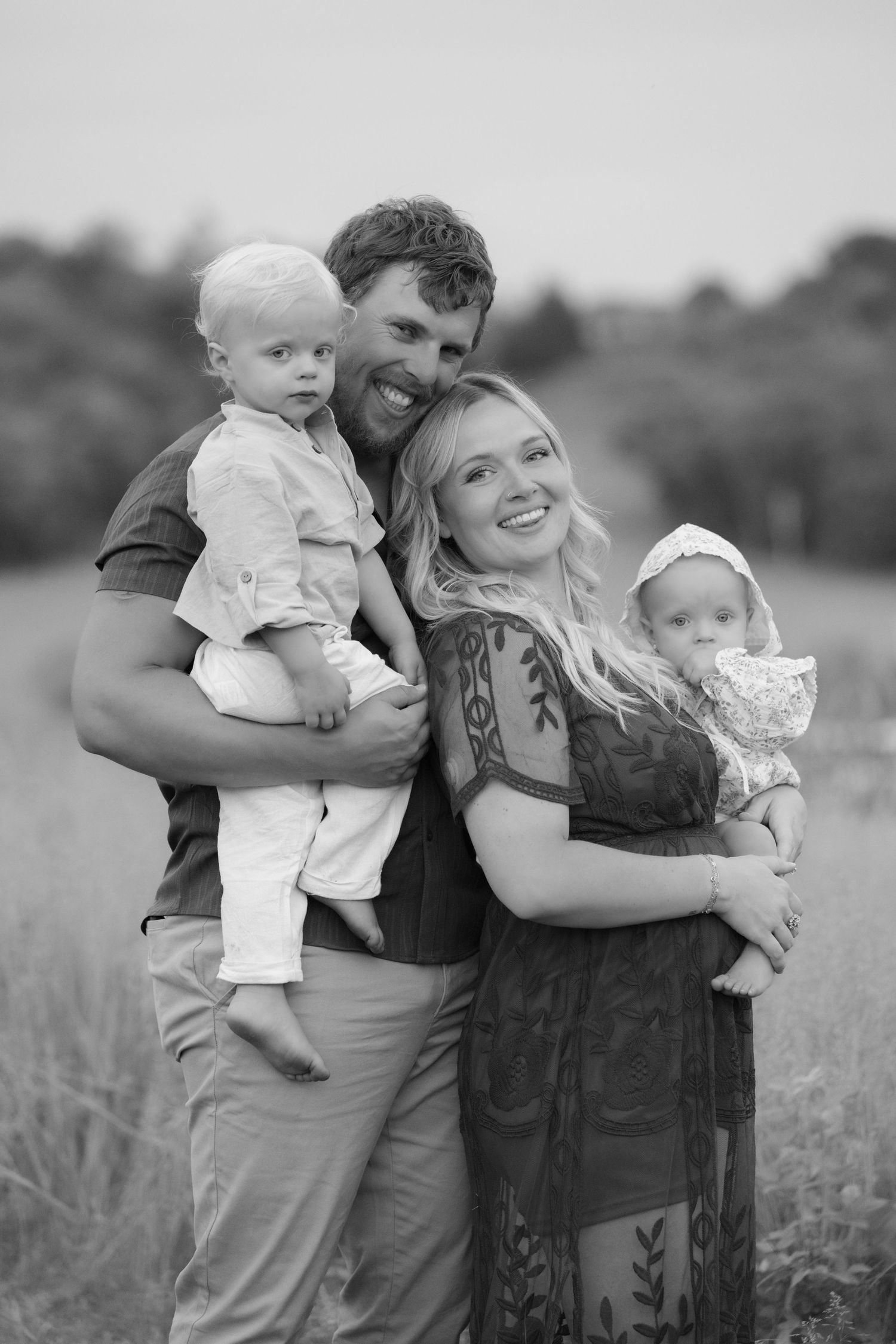 Mom leans against dad while they hold their babies with rolling hills in the background during outdoor family photos in Hudson, WI.
