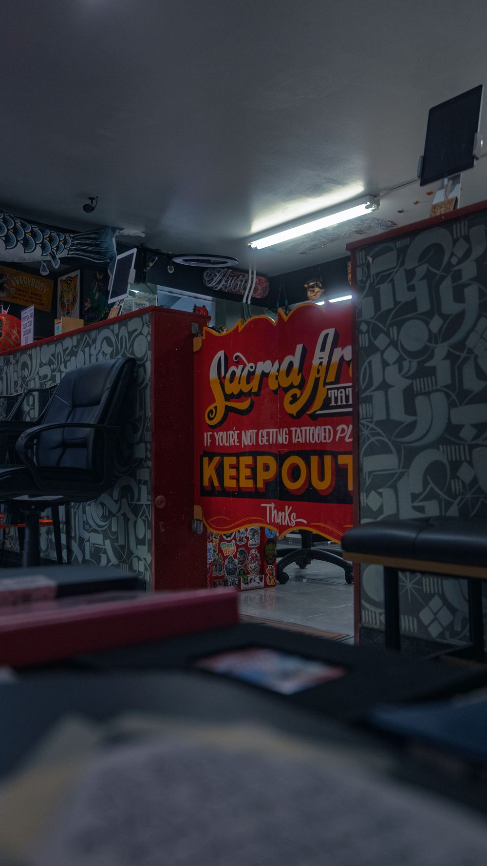 Interior of Sacred Art Tattoo in Honolulu, Hawaii, a hand-painted shop sign and "keep out" panel behind an empty station chair and desk.