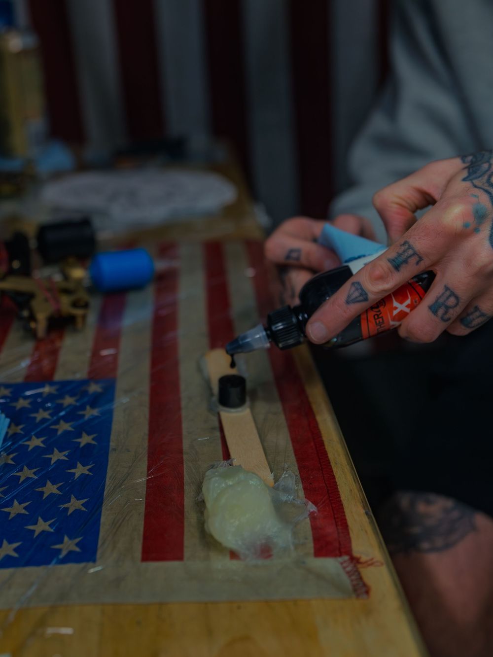 Karl Cooper's tattooed hands squeeze black ink onto a stick at his flag-draped station at Sacred Art Tattoo in Honolulu, Hawaii.
