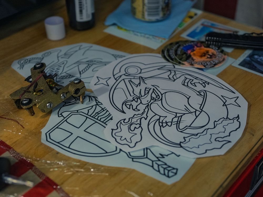 Line-drawing tattoo stencils and a brass coil machine laid out on Karl Cooper's flag-draped station at Sacred Art Tattoo in Honolulu, Hawaii