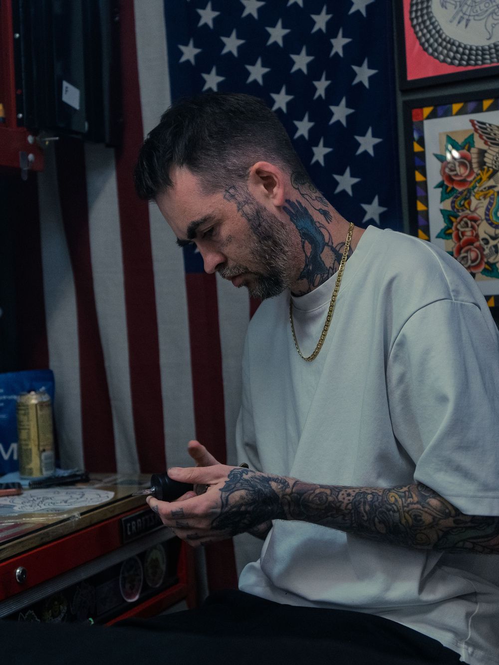 Tattoo artist Karl Cooper preps his machine at his station at Sacred Art Tattoo in Honolulu, Hawaii, a large American flag behind him.