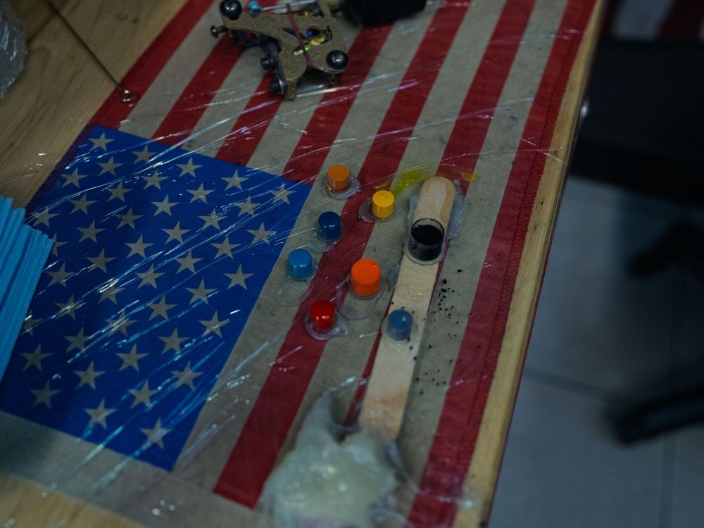 Ink caps in orange, blue, red and black lined up on a plastic-wrapped flag station at Sacred Art Tattoo in Honolulu, Hawaii, machine above.