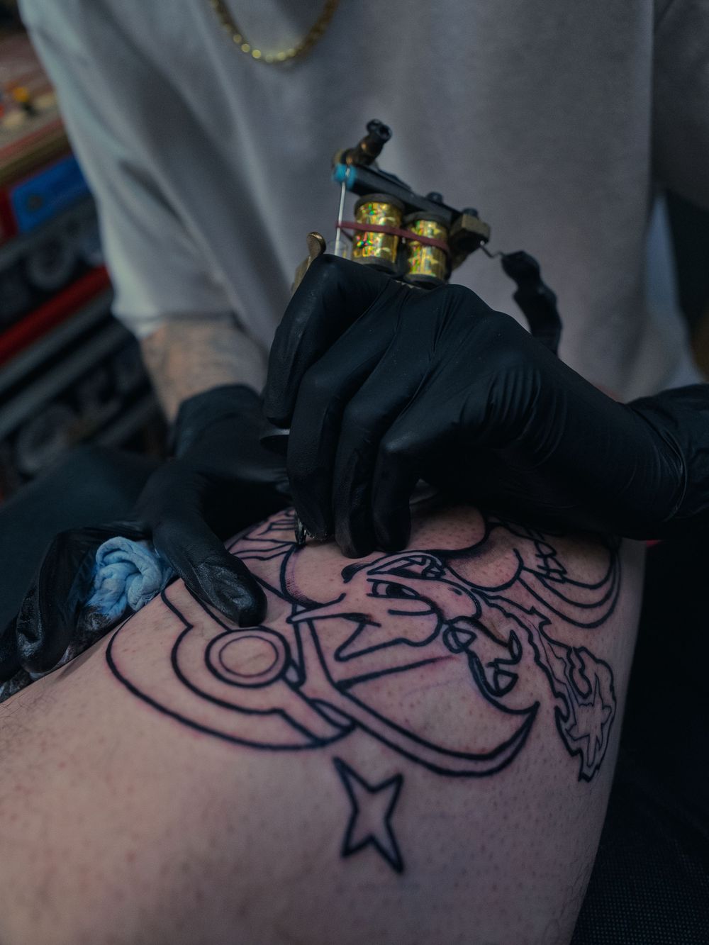Karl Cooper lays the black outline of an anchor-and-star leg tattoo with a coil machine at Sacred Art Tattoo in Honolulu, Hawaii.