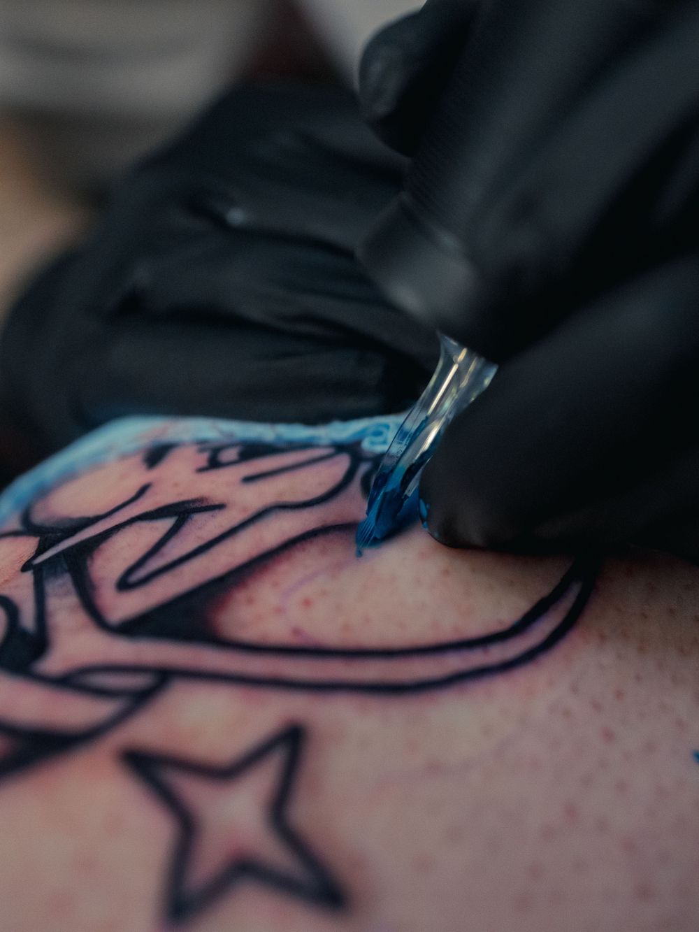 Macro shot of Karl Cooper packing bright blue ink into a bold black-lined leg tattoo at Sacred Art Tattoo in Honolulu, Hawaii, star nearby.