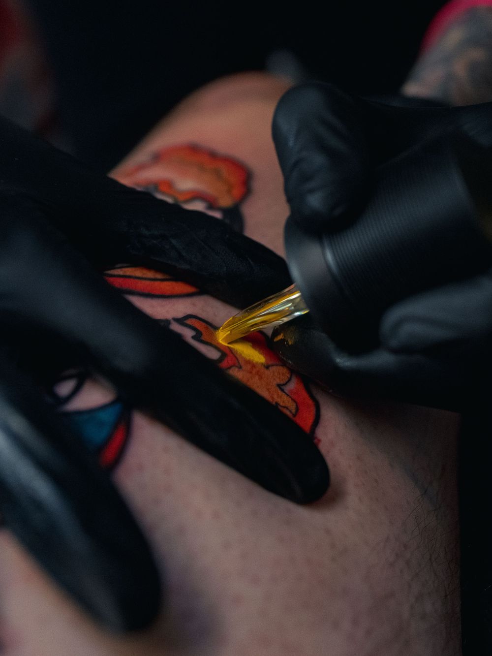Macro shot of Karl Cooper packing yellow ink into a fiery orange-and-red leg tattoo at Sacred Art Tattoo in Honolulu, Hawaii, tip to skin.