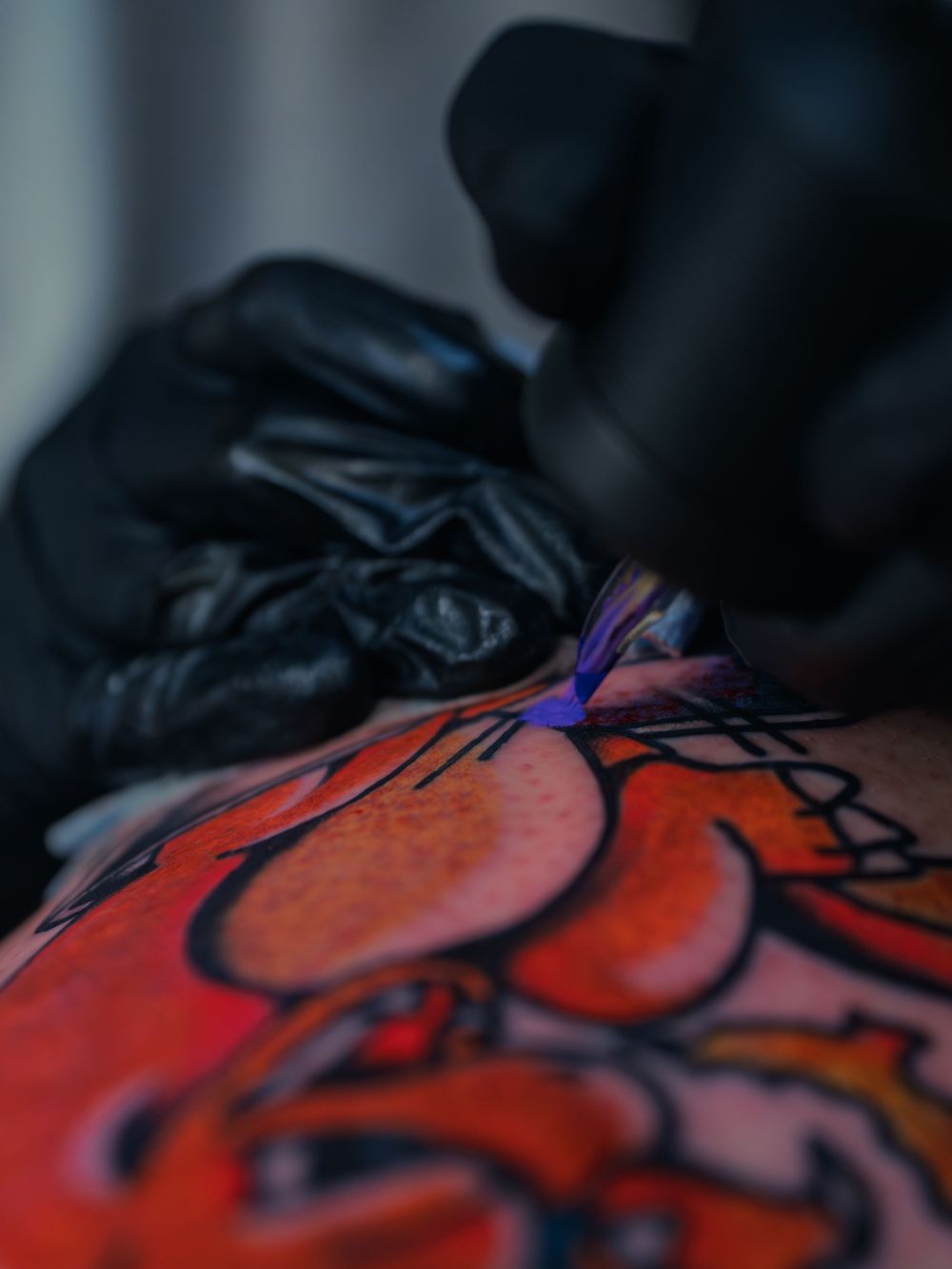 Macro shot of Karl Cooper's needle laying purple ink into a bold orange-and-black leg tattoo at Sacred Art Tattoo in Honolulu, Hawaii.