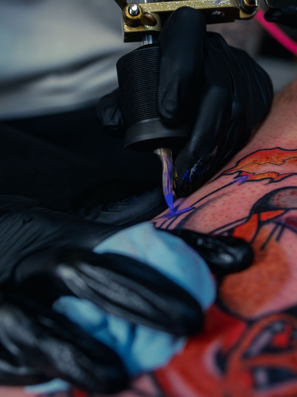 Close-up of Karl Cooper packing purple ink into a bold orange-and-black leg tattoo at Sacred Art Tattoo in Honolulu, Hawaii, needle to skin.