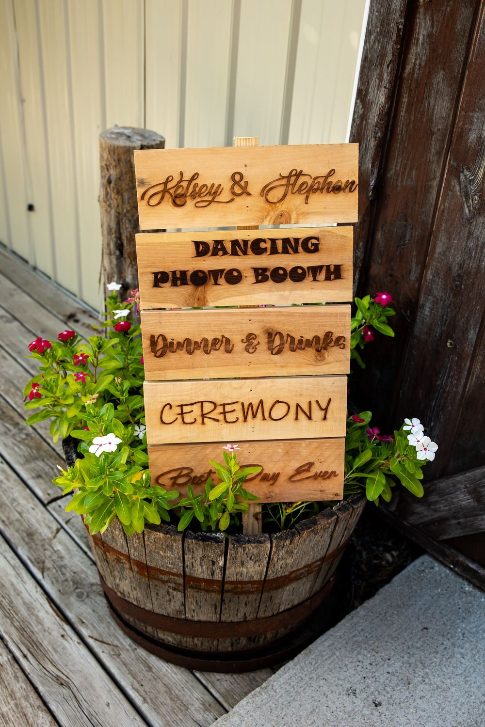 Rustic wooden wedding sign for Kelsey & Stephen in a barrel planter, listing dancing, photo booth, dinner, and ceremony.