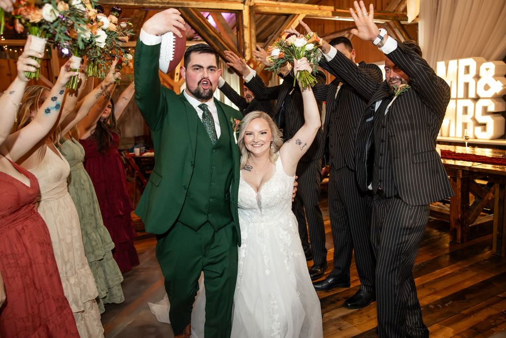 Bride and groom celebrate wedding reception grand entrance with raised hands, green suit, white gown, and MR & MRS sign.