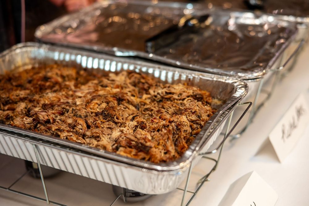 Catered pulled pork served in aluminum foil trays on warming stands at a buffet event.
