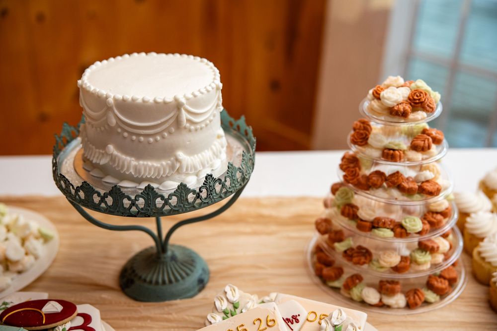 Elegant white wedding cake on green stand beside a tiered cupcake tower with orange frosting on a wooden table.