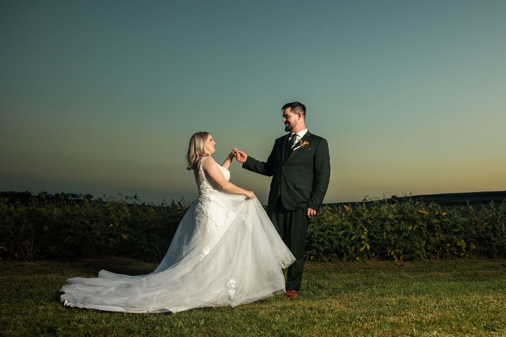 Bride and groom hold hands at sunset in a vineyard, bride in white gown, groom in dark suit.