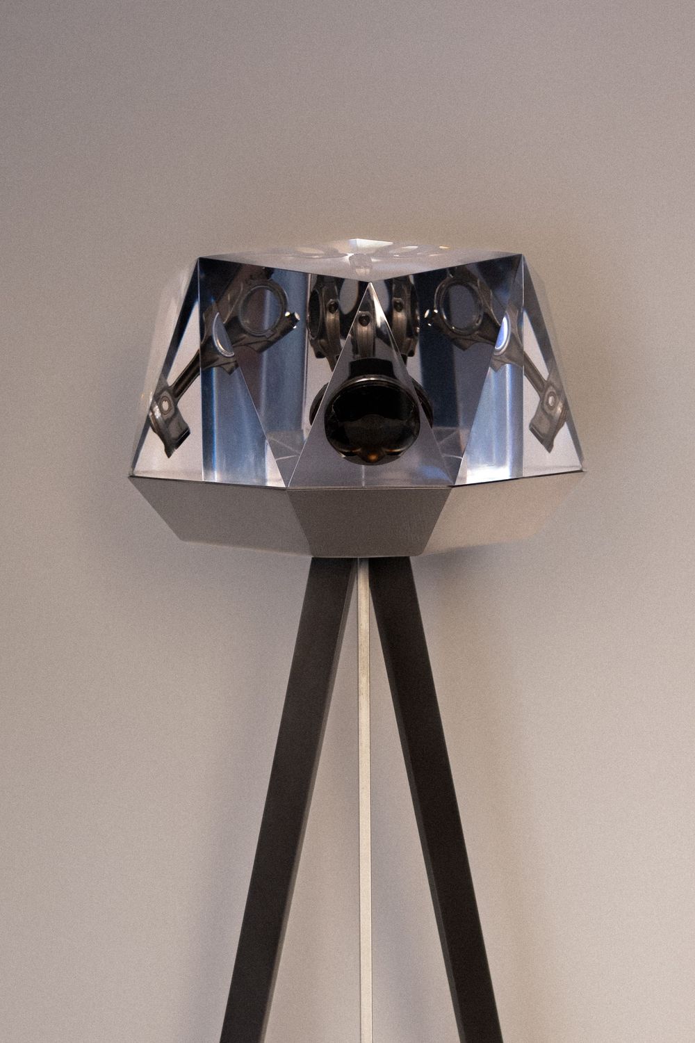 Modern geometric chrome floor lamp with tripod base and mirrored faceted shade on gray background.
