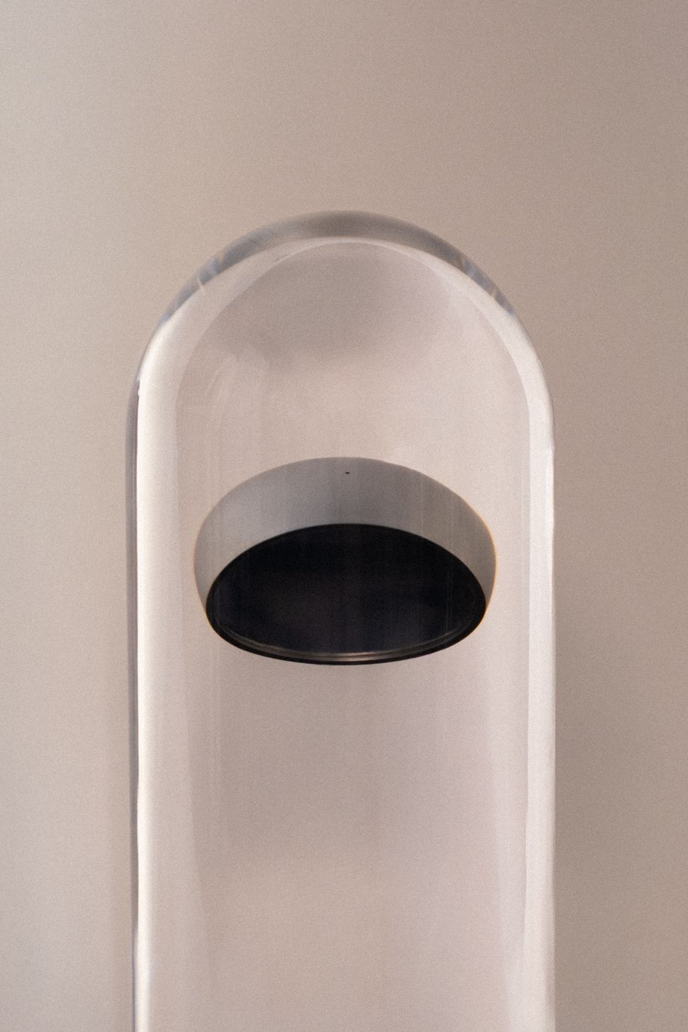 Clear acrylic dome sculpture with an oval black recessed opening, modern minimalist art piece on neutral background.