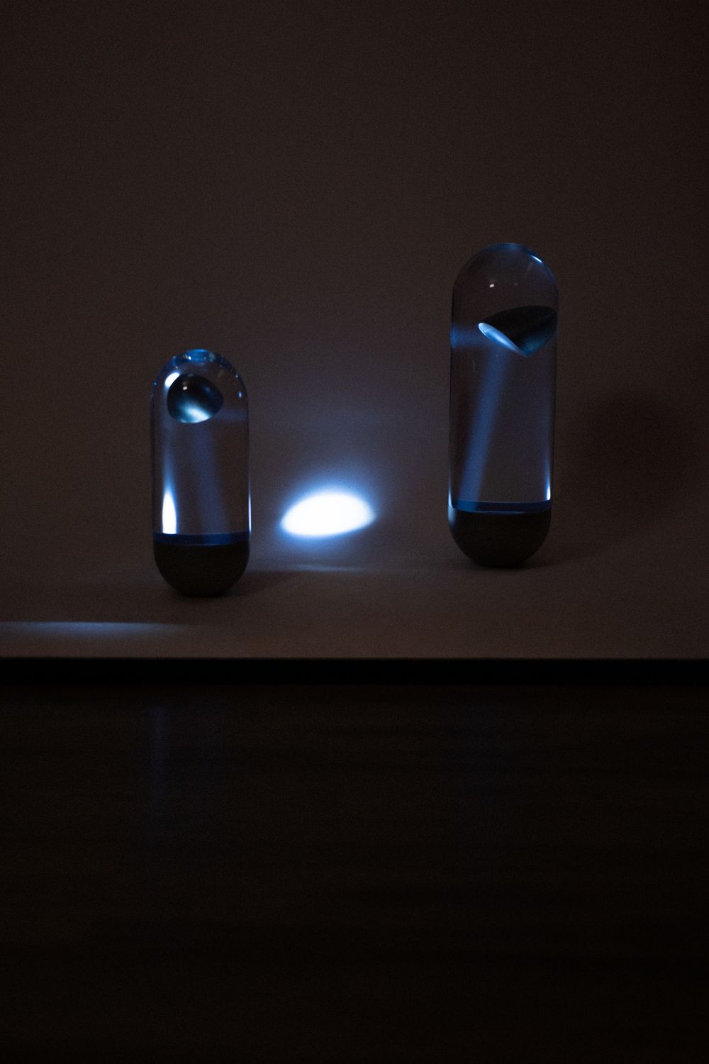 Two metallic capsule-shaped flashlights on a wooden shelf, one emitting a bright white light beam in a dark room.