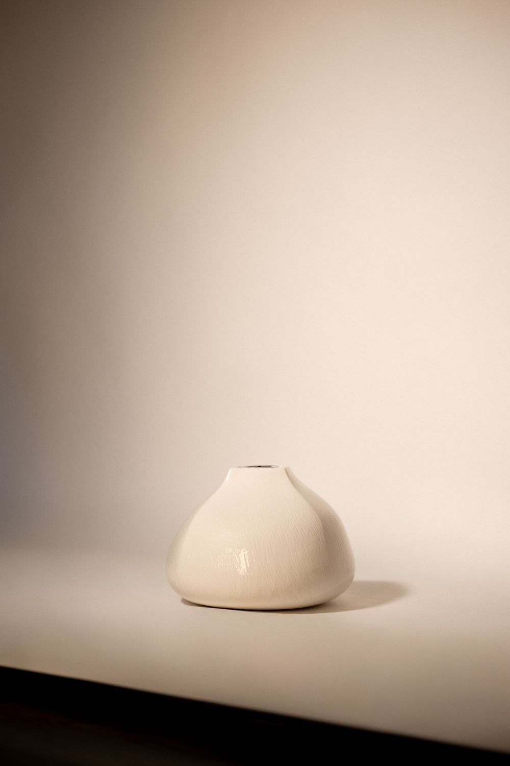Small white ceramic bud vase with smooth rounded shape and narrow opening, displayed on a neutral surface.