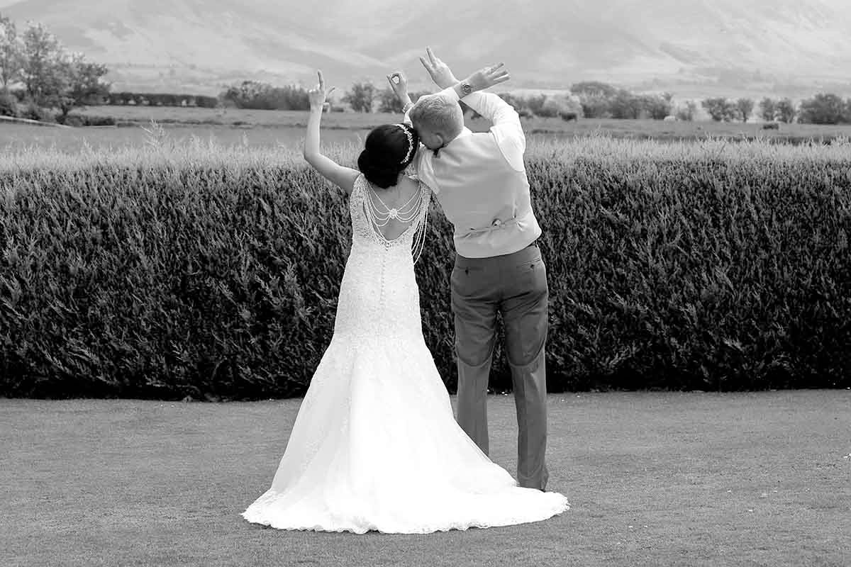 Black and white photo of a bride and groom celebrating with raised arms on their wedding day on the lawn at Hundith Hill Cockermouth