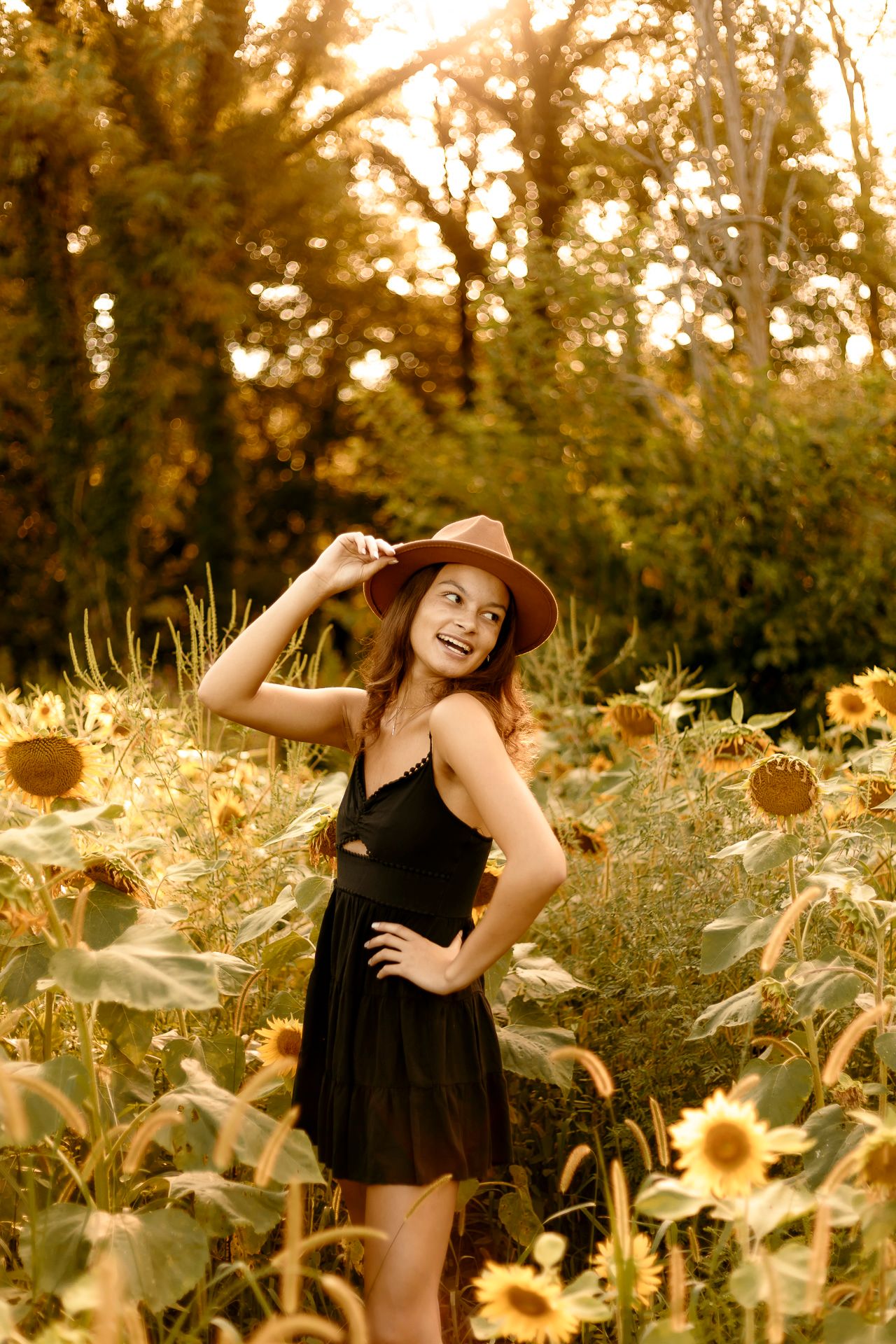 Young woman in floral dress posing on stone bridge with river and trees in golden hour light.