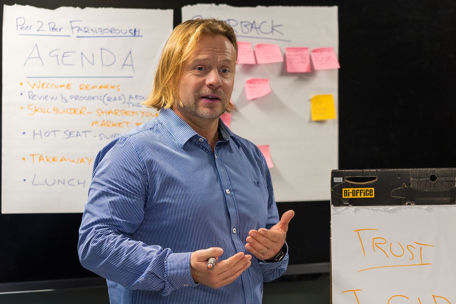 Man presenting at business workshop with agenda whiteboard and sticky notes.