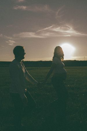Silhouette of a couple holding hands in a field at sunset, with a glowing sun behind them.