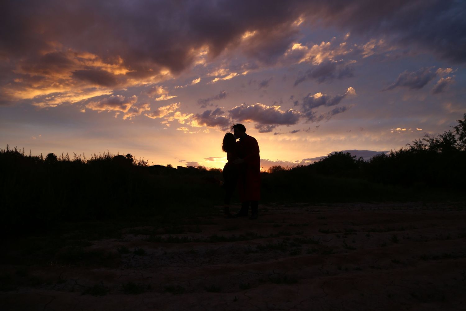 The silhouette of a couple embracing beneath a dramatic purple and orange sunset sky.
