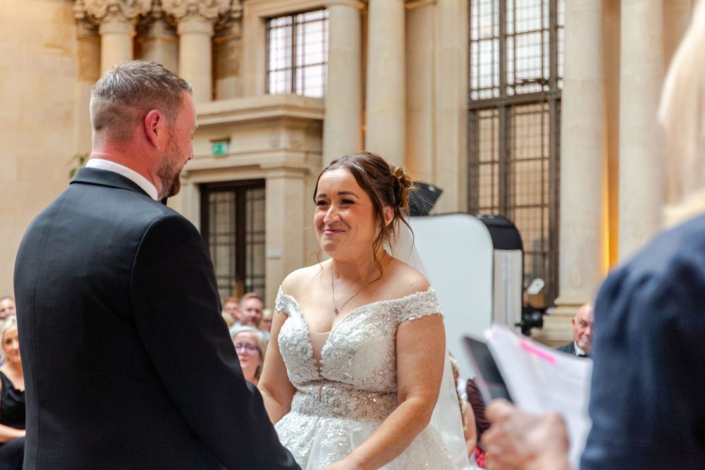 Bride smiling joyfully at groom during wedding ceremony in elegant grand hall venue.