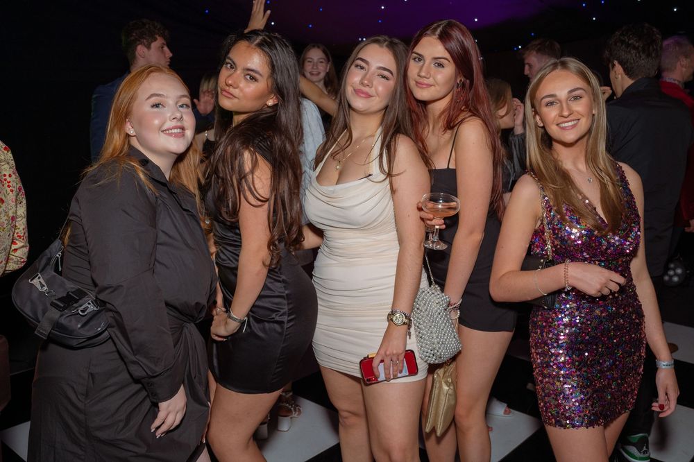 Five young women posing together at a nightclub, dressed in stylish outfits, smiling for the camera.