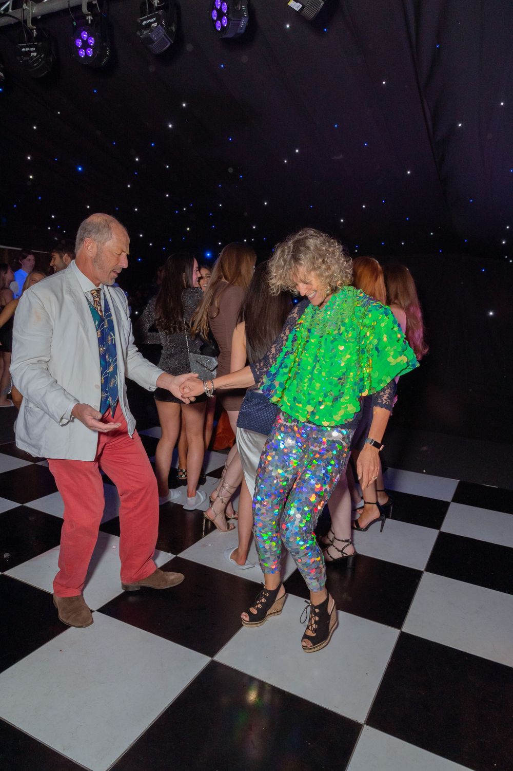 Two adults dancing on a black and white checkered dance floor at a vibrant nightclub party event.
