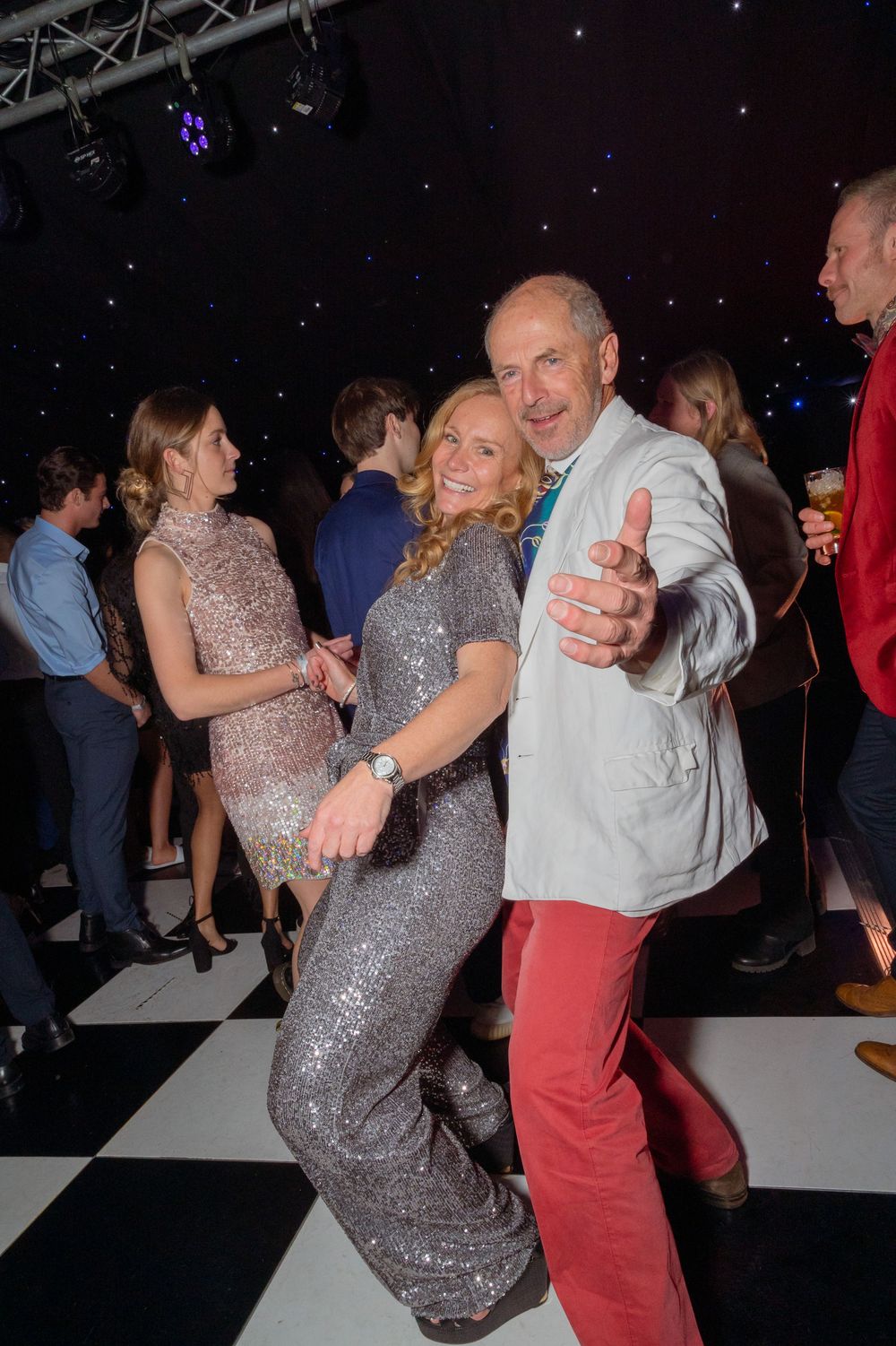 Couple dancing joyfully in sequin outfits on a checkered dance floor at a glamorous party event.