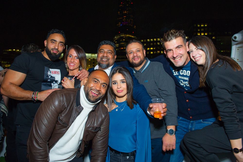 Group of friends posing together at an outdoor nighttime social event with city lights in the background.