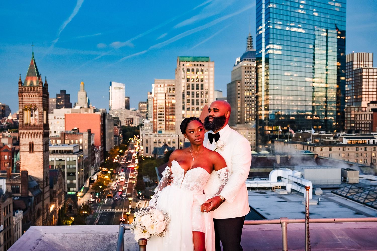 Newlywed couple posing on the hotel lenox rooftop with the Boston skyline backdrop at dusk.