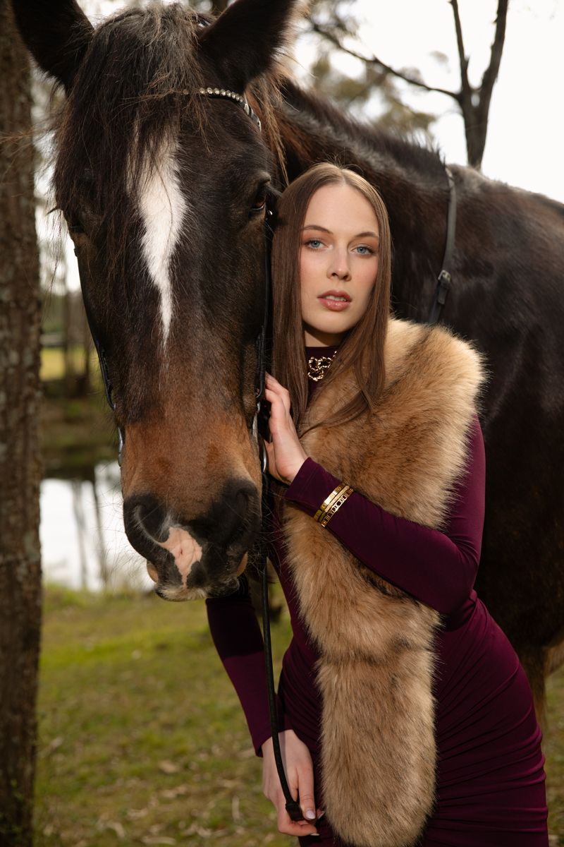 Young woman in burgundy velvet dress and fur stole poses with dark horse outdoors in winter setting photoshoot with a horse in sydney