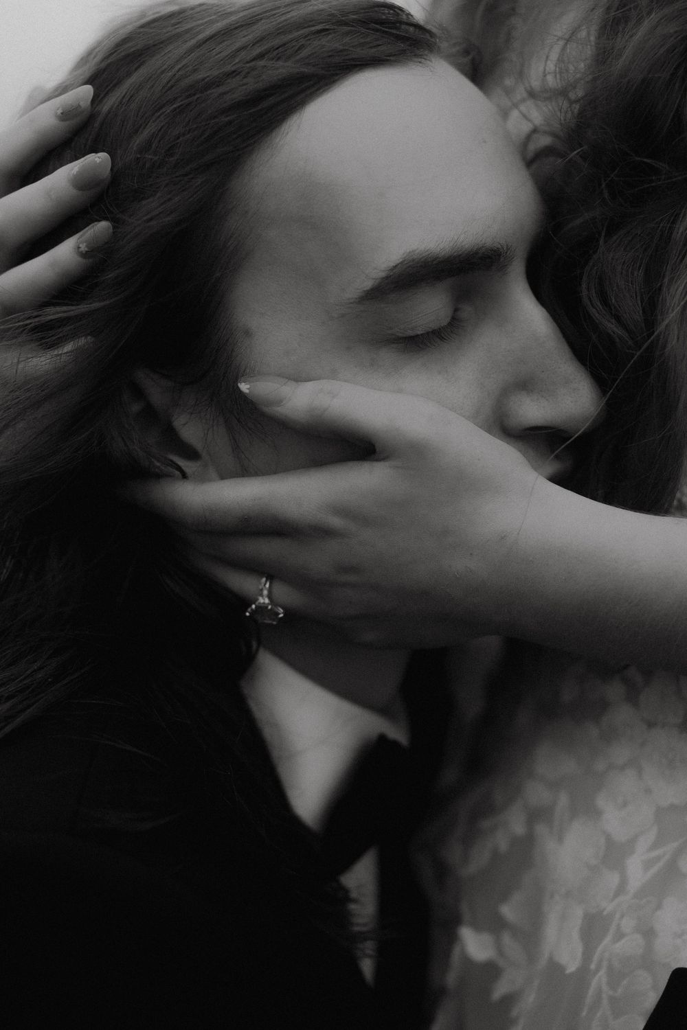 Black and white photo of a couple in an intimate embrace, woman's hand with engagement ring cradling man's face.