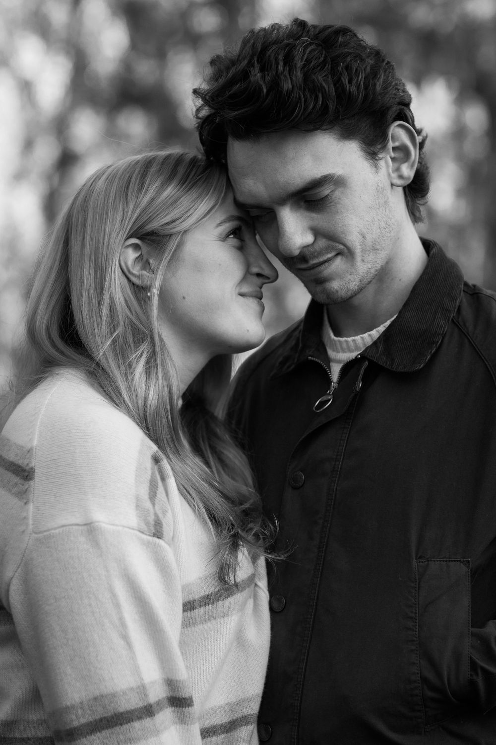 Black and white photo of a young romantic couple touching foreheads tenderly outdoors.