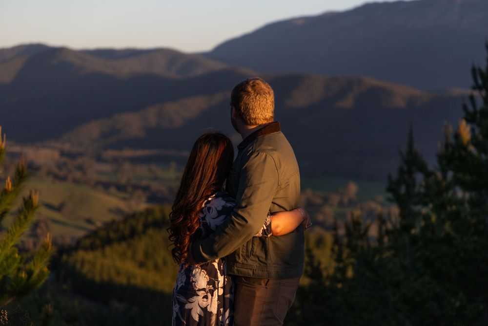Couple embracing while overlooking stunning mountain landscape at golden hour sunset.