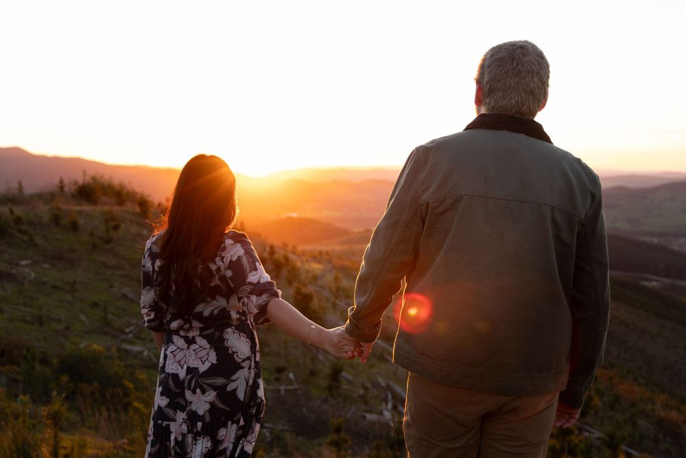 Couple holding hands watching a golden sunset over mountain landscape from a scenic overlook.