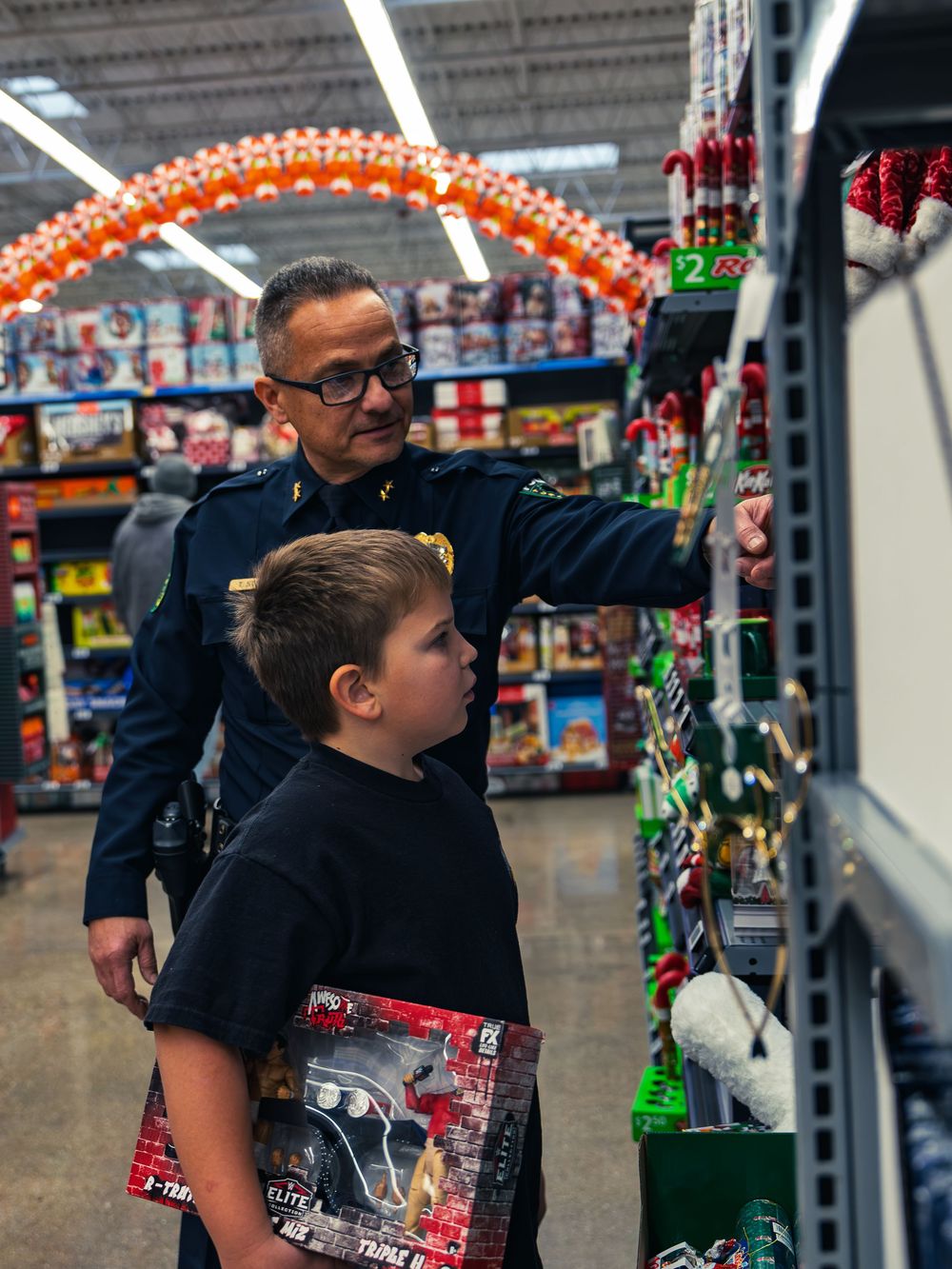 A police officer points out an item on the shelf to a young child holding a toy as they browse a holiday aisle together at the event.