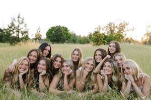 Group of smiling young women posing together in a sunlit grassy field during golden hour.