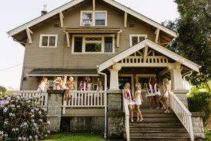 Group of women in white robes gathered on the porch and steps of a charming craftsman-style house.