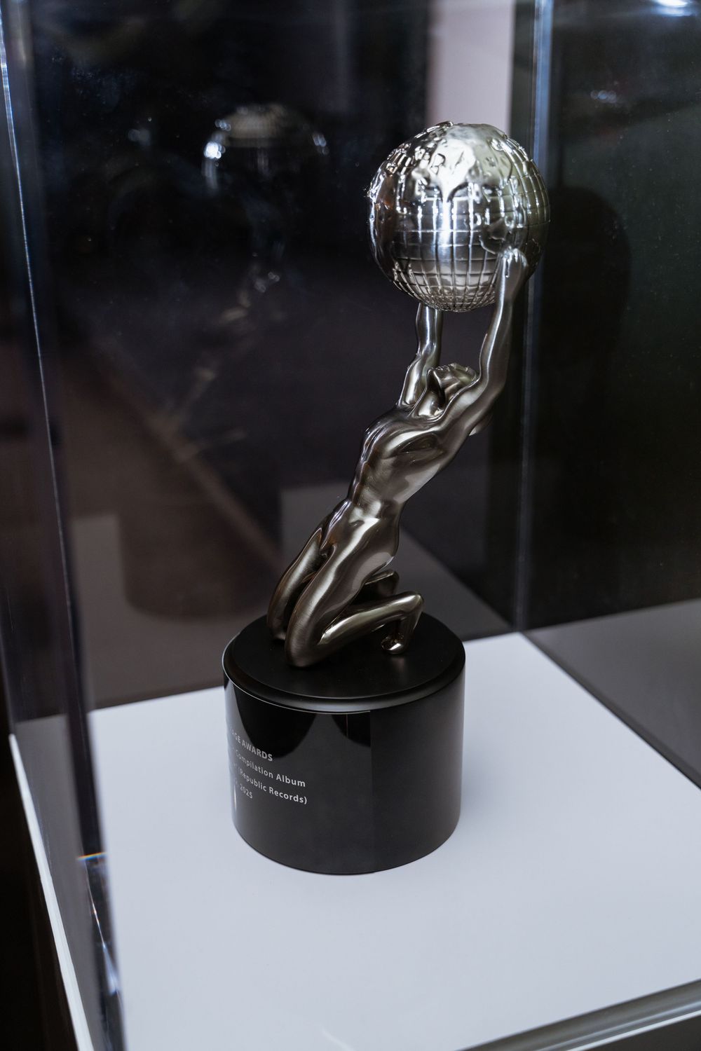 Silver trophy statue of a figure holding a globe, displayed in a glass case on a black cylindrical base.