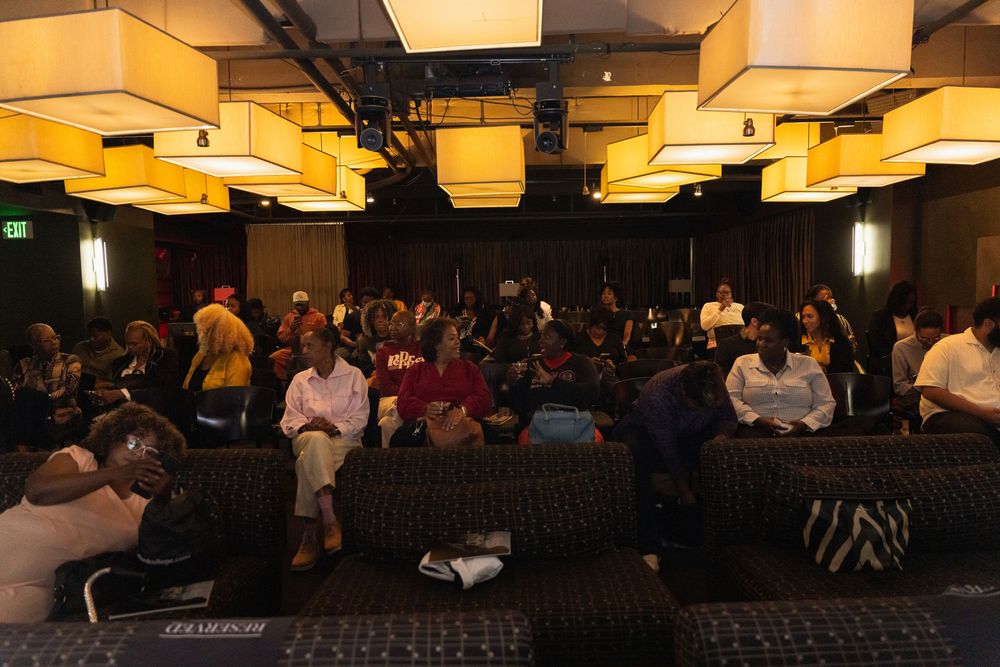 Diverse audience seated in a dimly lit event venue with warm overhead lighting during a presentation.