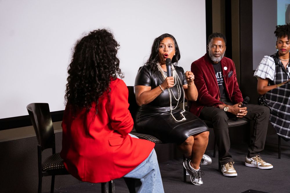 Panel discussion with four people seated, one speaking into a microphone at a film screening event.